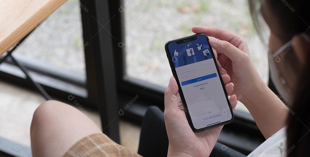 Mulher segurando um iPhone X com serviço social de Internet Facebook na tela.