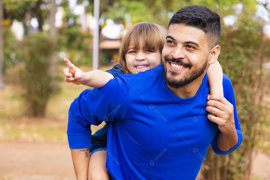 Pai e filha sorrindo para a câmera no parque. Filha sobe nas costas do papai. Feliz dia dos pais