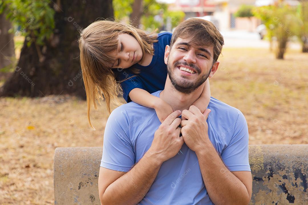 Pai e filha sorrindo para a câmera no parque. Filha sobe nas costas do papai. Feliz dia dos pais