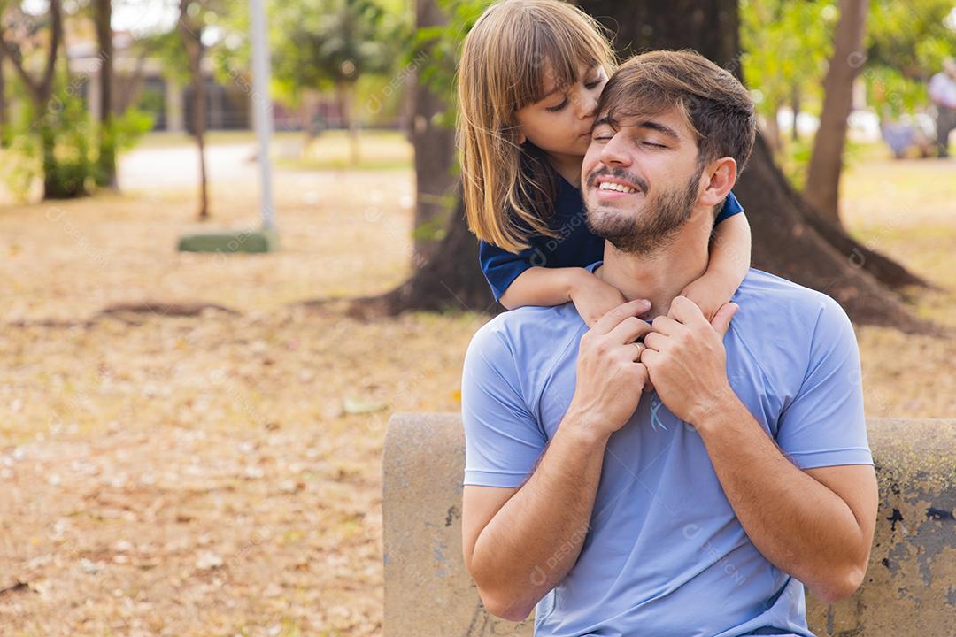 Pai e filha sorrindo para a câmera no parque. Filha sobe nas costas do papai. Feliz dia dos pais