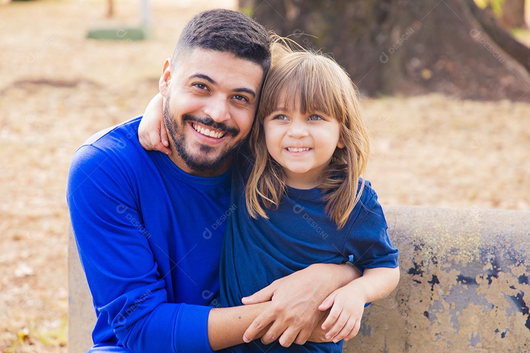Pai e filha sorrindo para a câmera no parque. Filha sobe nas costas do papai. Feliz dia dos pais