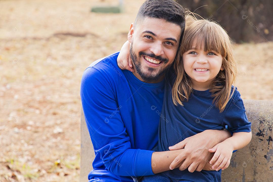 Pai e filha sorrindo para a câmera no parque. Filha sobe nas costas do papai. Feliz dia dos pais