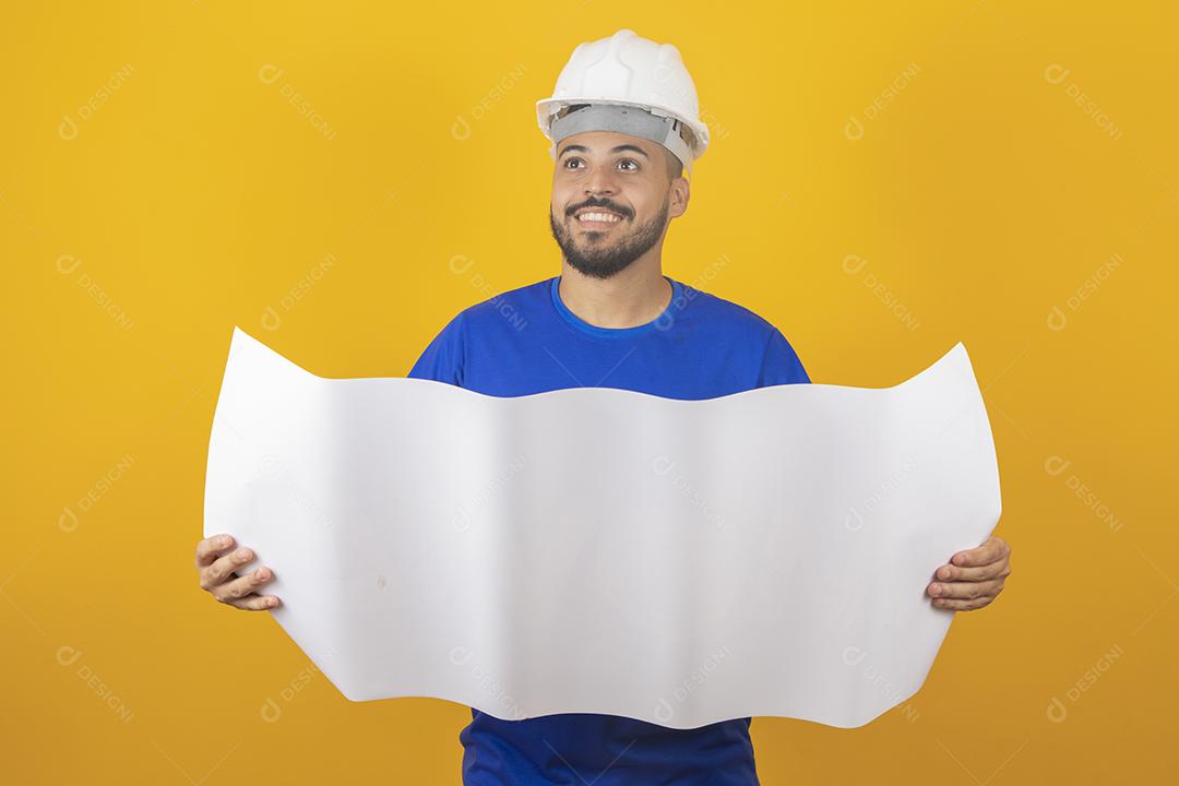 Homem jovem arquiteto com capacete segurando planta de construção isolada sobre fundo amarelo