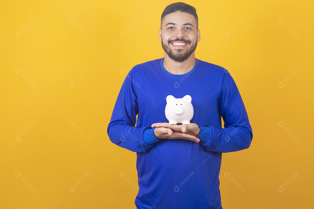 Jovem bonito sobre fundo amarelo isolado segurando um grande cofrinho