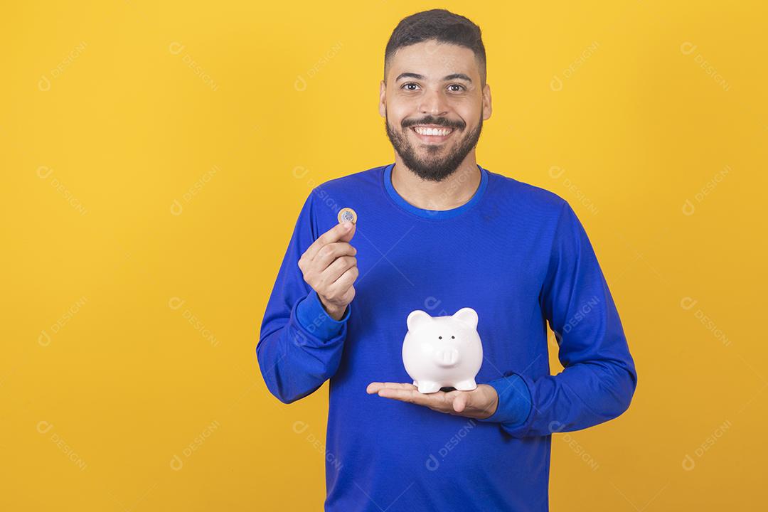 Jovem bonito sobre fundo amarelo isolado segurando um grande cofrinho