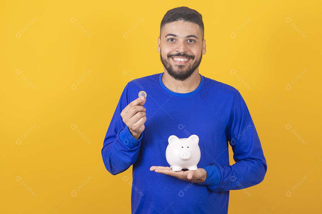 Jovem bonito sobre fundo amarelo isolado segurando um grande cofrinho