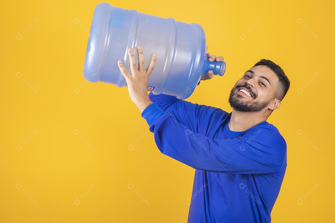 Rapaz com grande galão de água bebendo em fundo amarelo