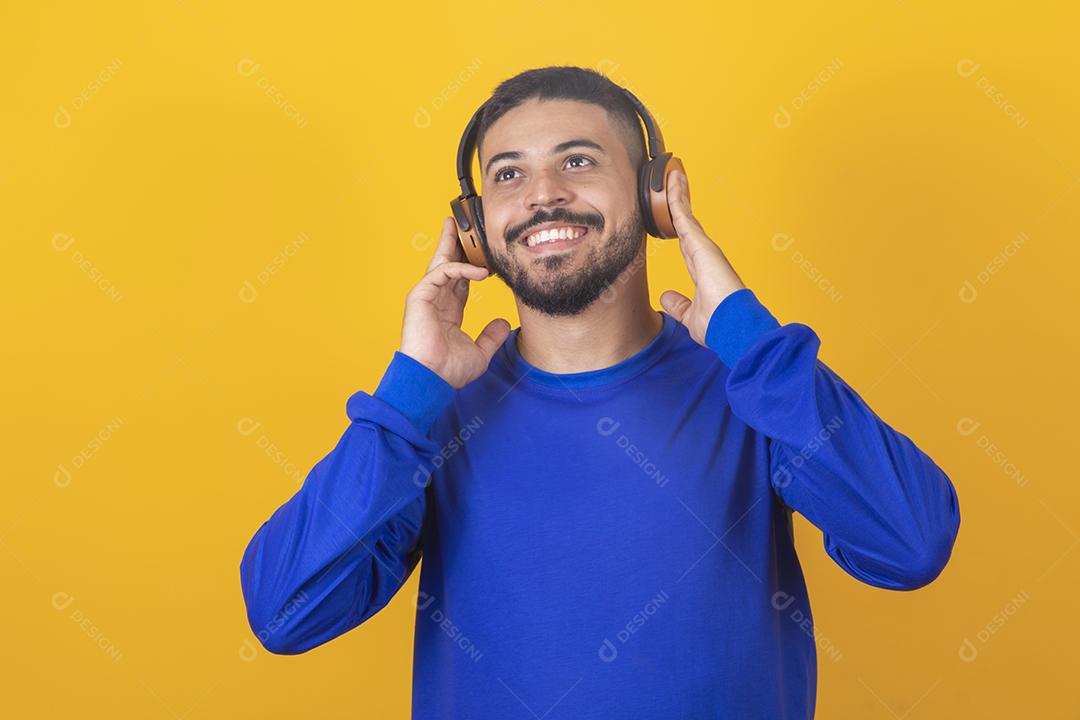 jovem bonito ouvindo música em fones de ouvido, fundo de estúdio amarelo, isolado, sorrindo, feliz