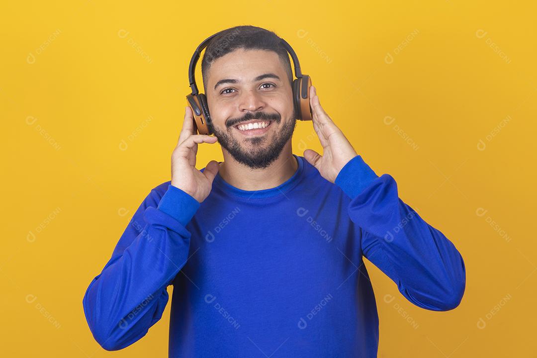 jovem bonito ouvindo música em fones de ouvido, fundo de estúdio amarelo, isolado, sorrindo, feliz