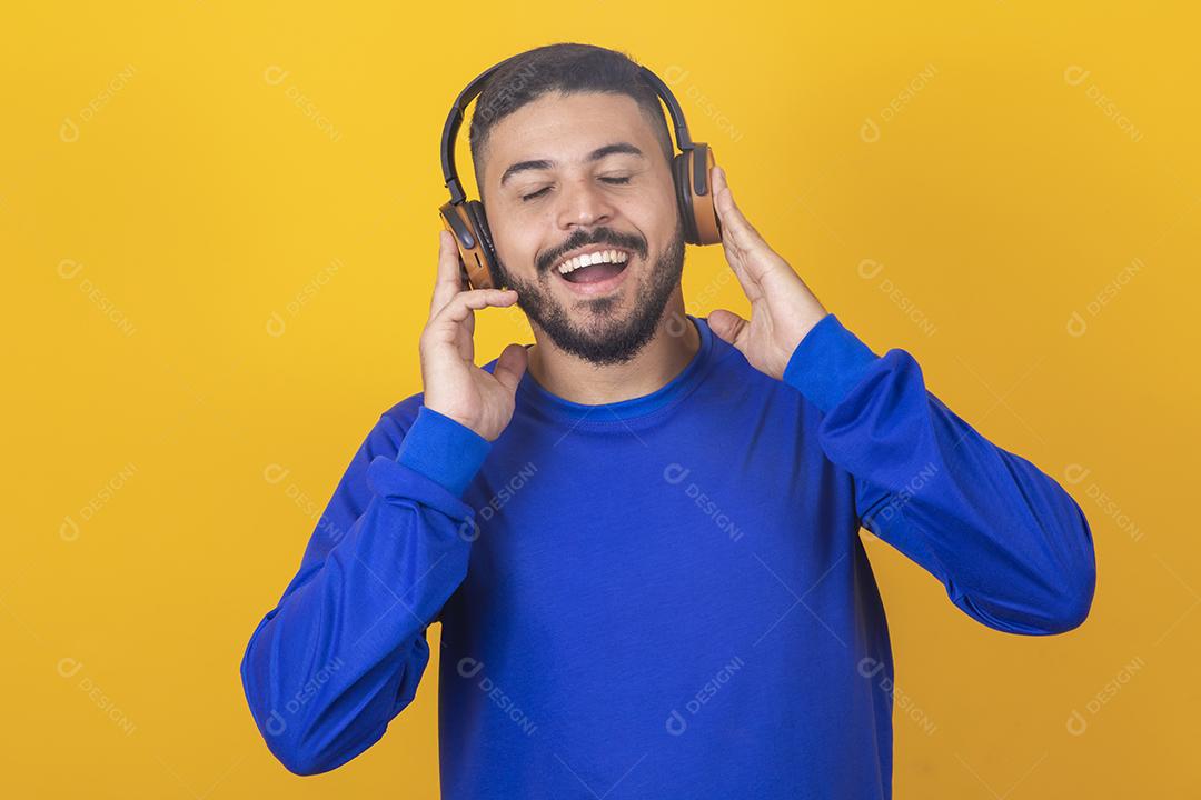 jovem bonito ouvindo música em fones de ouvido, fundo de estúdio amarelo, isolado, sorrindo, feliz