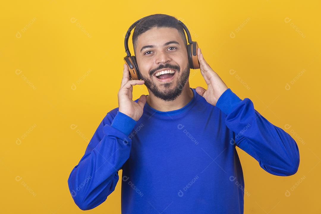 jovem bonito ouvindo música em fones de ouvido, fundo de estúdio amarelo, isolado, sorrindo, feliz
