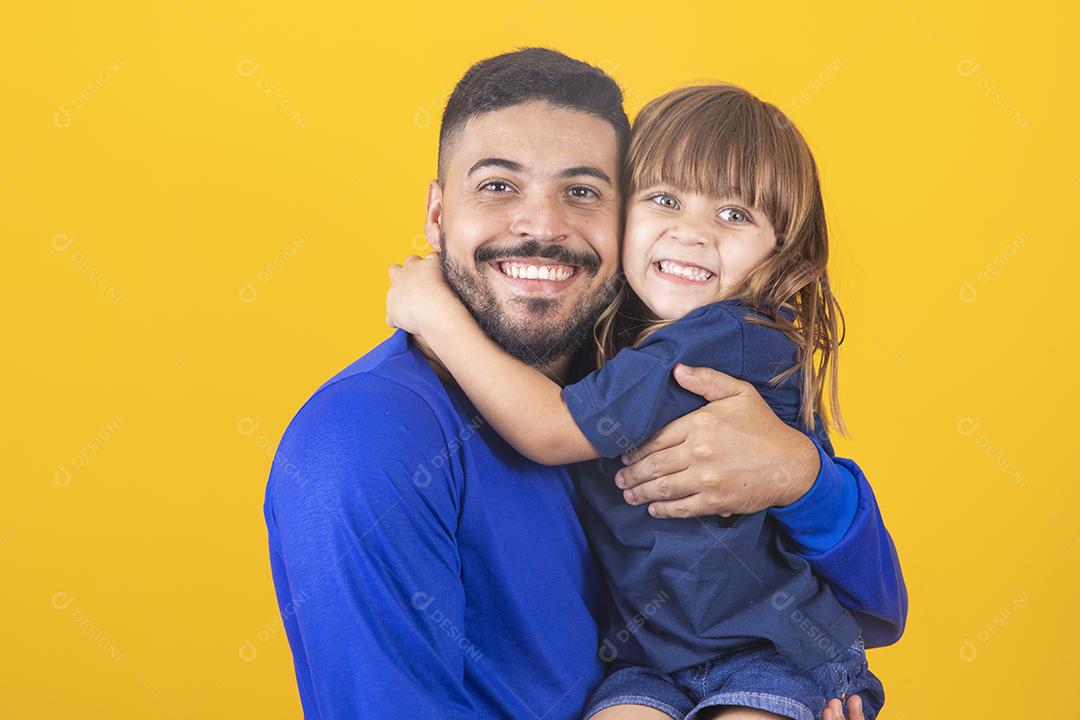 jovem rapaz bonito com sua filha em fundo amarelo, abraçando-o. Filha e pai abraçando em fundo colorido
