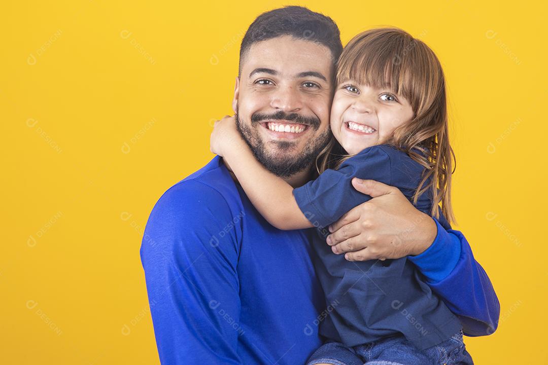 jovem rapaz bonito com sua filha em fundo amarelo, abraçando-o. Filha e pai abraçando em fundo colorido
