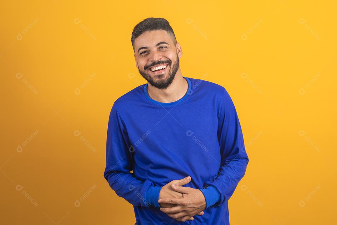 Jovem rapaz bonito explode de rir em fundo isolado. Homem ri tanto que seu estômago dói