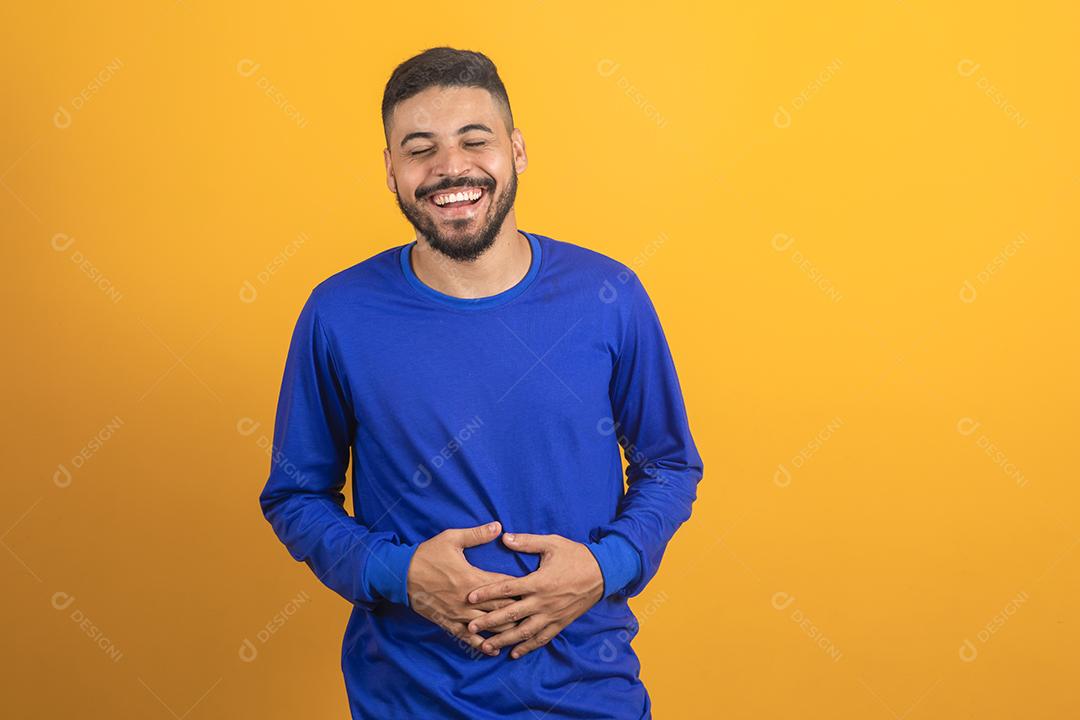 Jovem rapaz bonito explode de rir em fundo isolado. Homem ri tanto que seu estômago dói