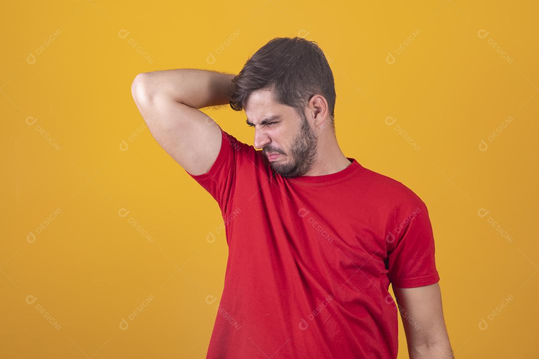 Homem de camiseta cheira as axilas, incomodado com o problema da transpiração fétida e odor corporal