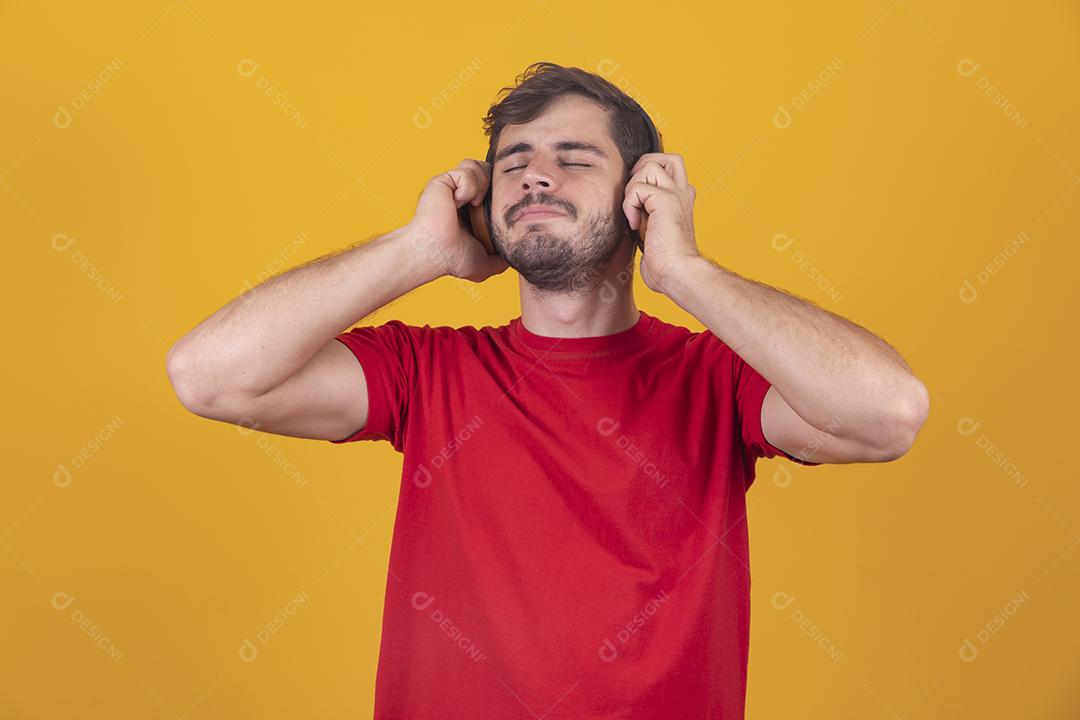 jovem bonito ouvindo música em fones de ouvido, fundo de estúdio amarelo, isolado, sorrindo, feliz