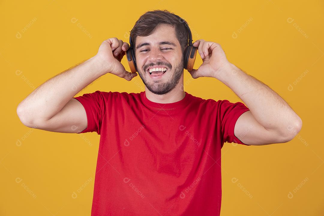 jovem bonito ouvindo música em fones de ouvido, fundo de estúdio amarelo, isolado, sorrindo, feliz