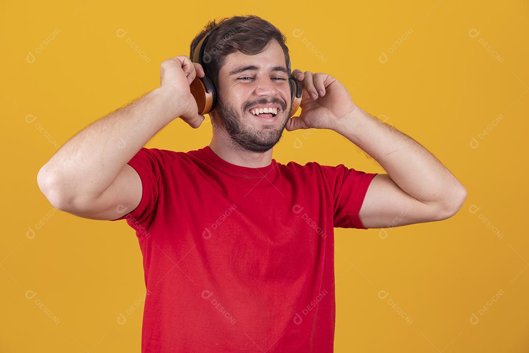 jovem bonito ouvindo música em fones de ouvido, fundo de estúdio amarelo, isolado, sorrindo, feliz