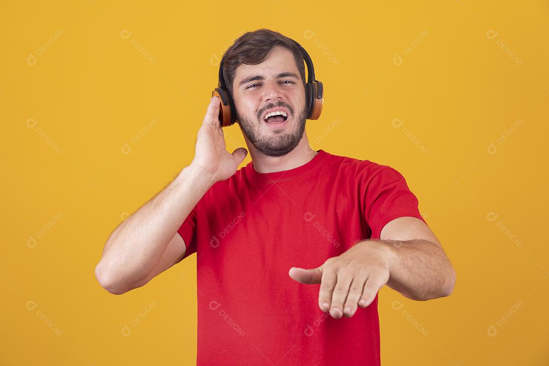 jovem bonito ouvindo música em fones de ouvido, fundo de estúdio amarelo, isolado, sorrindo, feliz