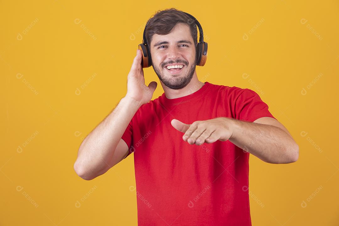 jovem bonito ouvindo música em fones de ouvido, fundo de estúdio amarelo, isolado, sorrindo, feliz
