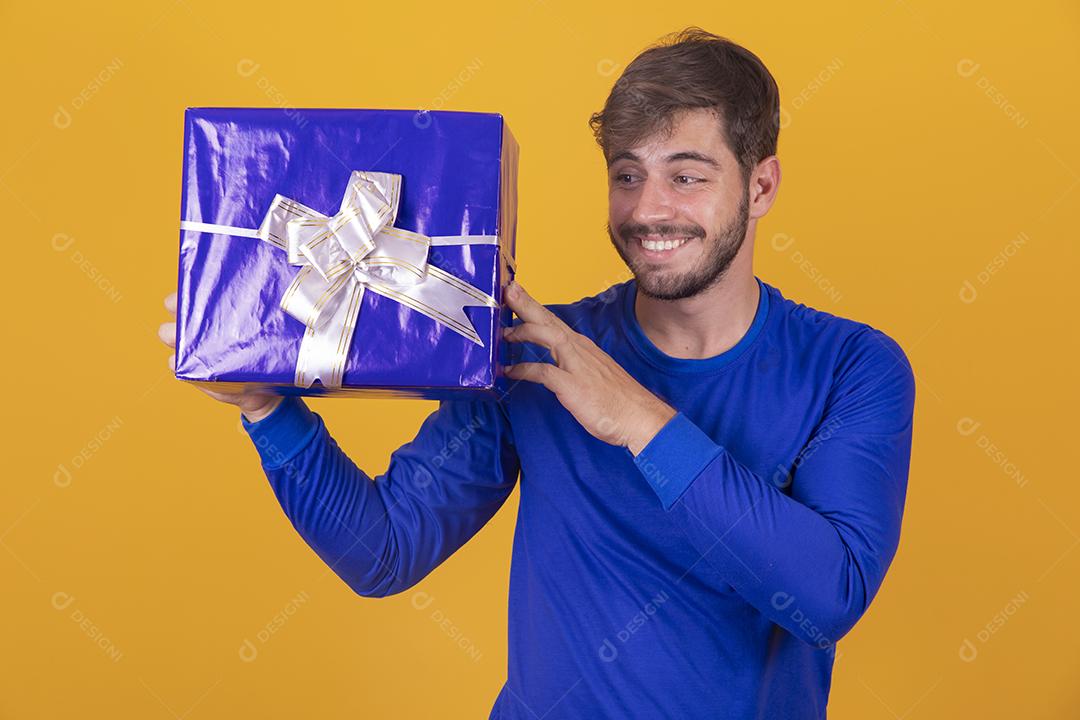 jovem sorridente segurando uma caixa de presente em fundo amarelo jovem segurando uma caixa de presente em fundo amarelo
