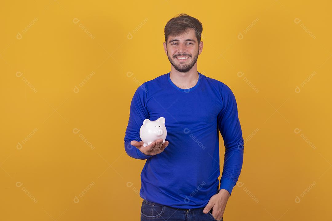 Jovem bonito sobre fundo amarelo isolado segurando um grande cofrinho