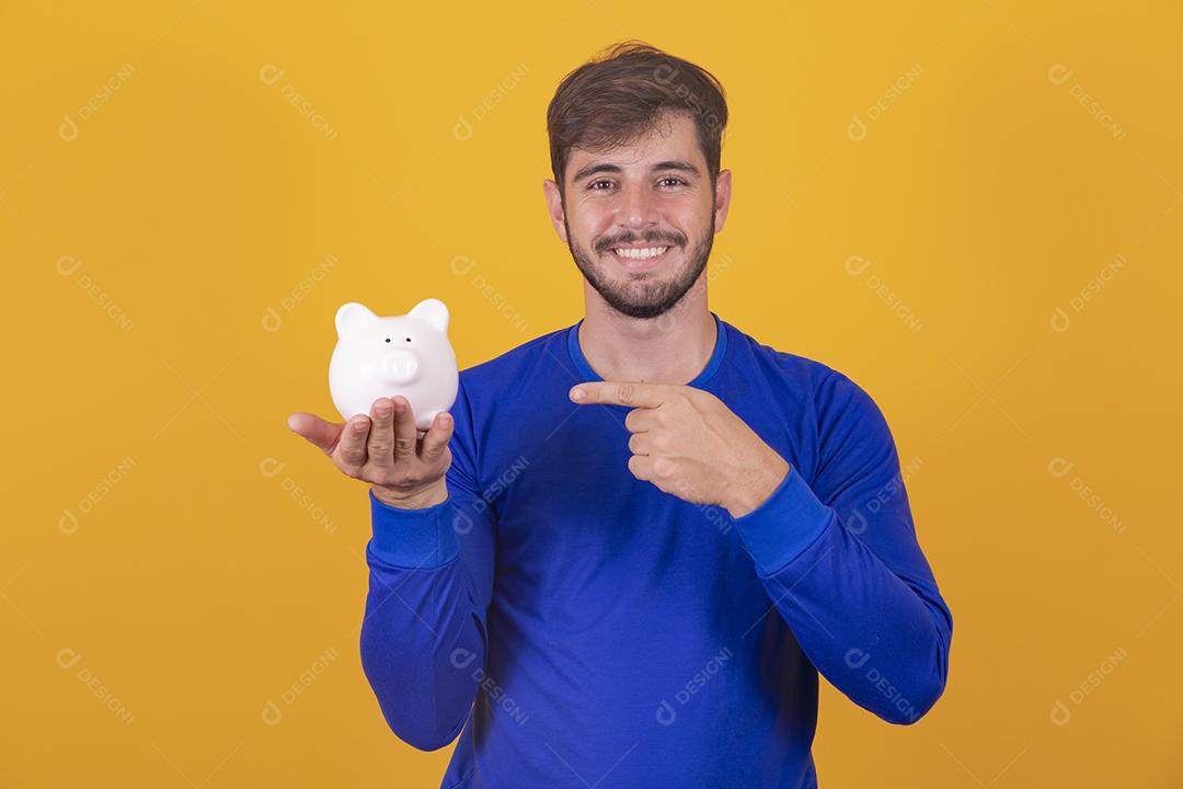 Jovem bonito sobre fundo amarelo isolado segurando um grande cofrinho