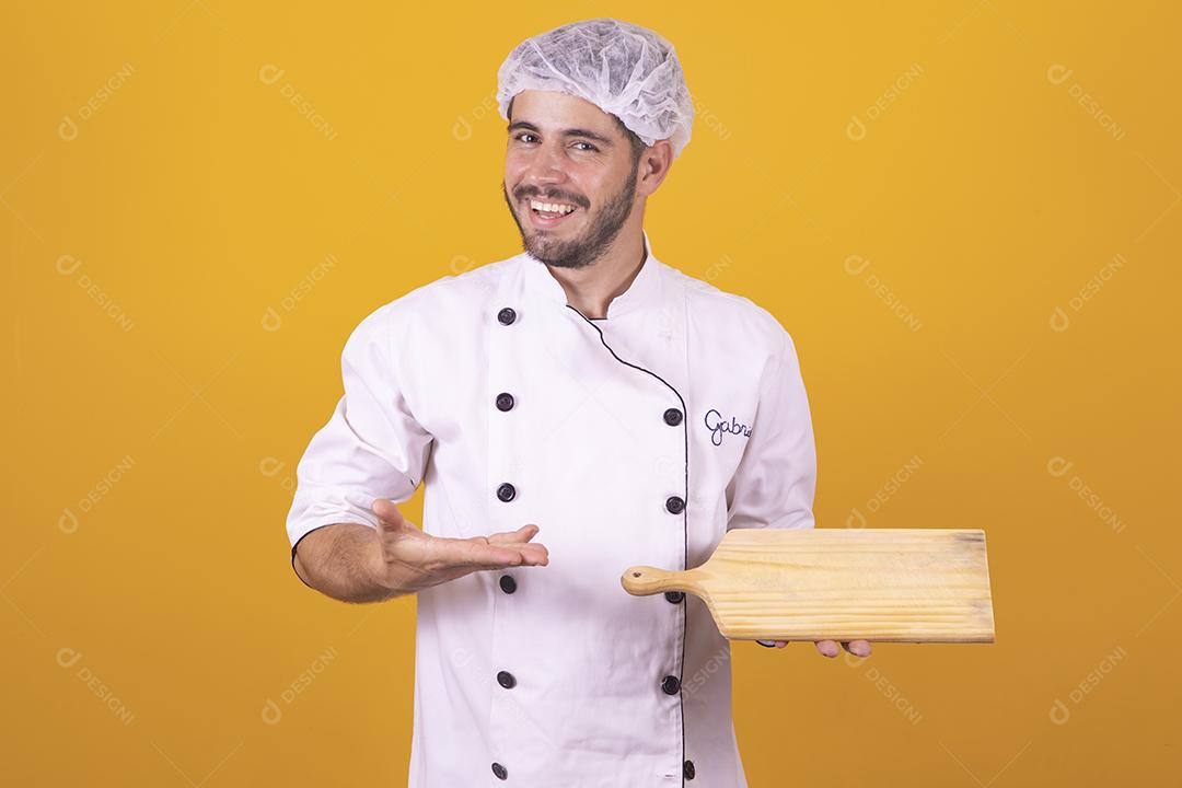 Sorrindo jovem chef masculino cozinheiro ou padeiro na camisa uniforme branca posando isolado no retrato de estúdio de fundo amarelo. Cozinhar o conceito de comida. Mock up espaço de cópia. Chicotear ovos batendo na tigela