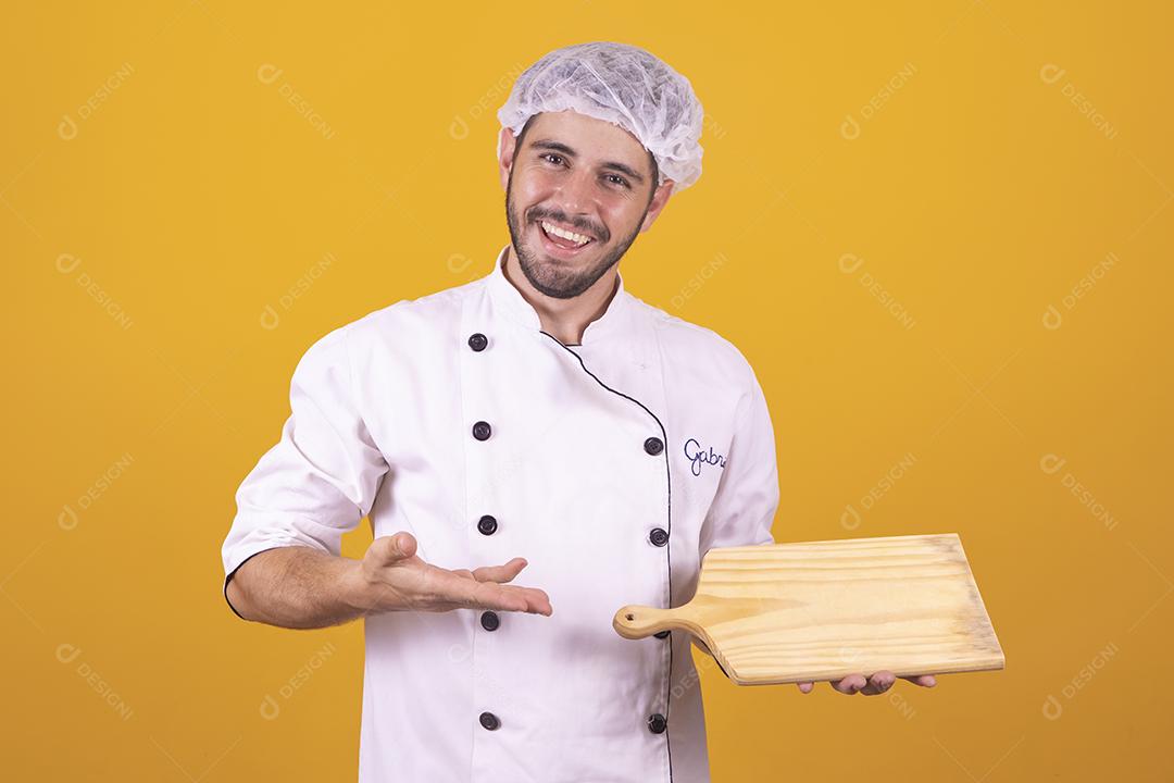 Sorrindo jovem chef masculino cozinheiro ou padeiro na camisa uniforme branca posando isolado no retrato de estúdio de fundo amarelo. Cozinhar o conceito de comida. Mock up espaço de cópia. Chicotear ovos batendo na tigela