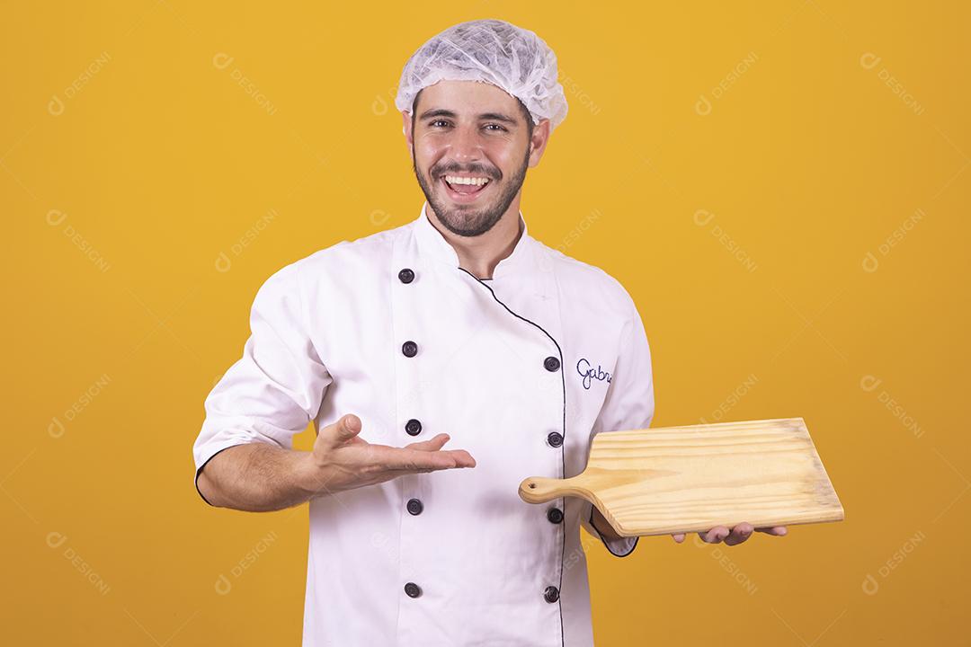 Sorrindo jovem chef masculino cozinheiro ou padeiro na camisa uniforme branca posando isolado no retrato de estúdio de fundo amarelo. Cozinhar o conceito de comida. Mock up espaço de cópia. Chicotear ovos batendo na tigela
