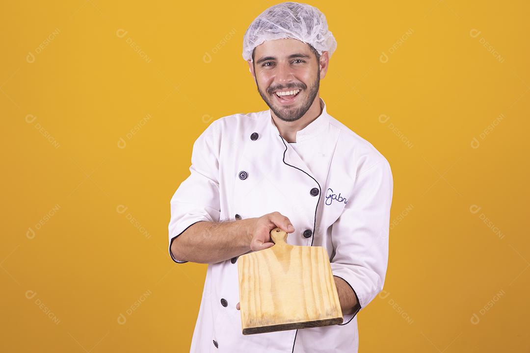 Sorrindo jovem chef masculino cozinheiro ou padeiro na camisa uniforme branca posando isolado no retrato de estúdio de fundo amarelo. Cozinhar o conceito de comida. Mock up espaço de cópia. Chicotear ovos batendo na tigela