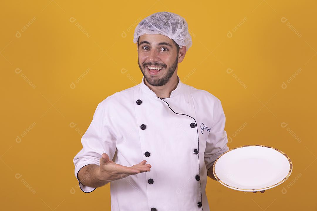 Sorrindo jovem chef masculino cozinheiro ou padeiro na camisa uniforme branca posando isolado no retrato de estúdio de fundo amarelo. Cozinhar o conceito de comida. Mock up espaço de cópia. Chicotear ovos batendo na tigela
