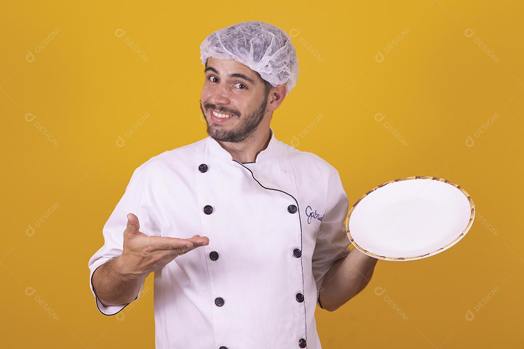 Sorrindo jovem chef masculino cozinheiro ou padeiro na camisa uniforme branca posando isolado no retrato de estúdio de fundo amarelo. Cozinhar o conceito de comida. Mock up espaço de cópia. Chicotear ovos batendo na tigela