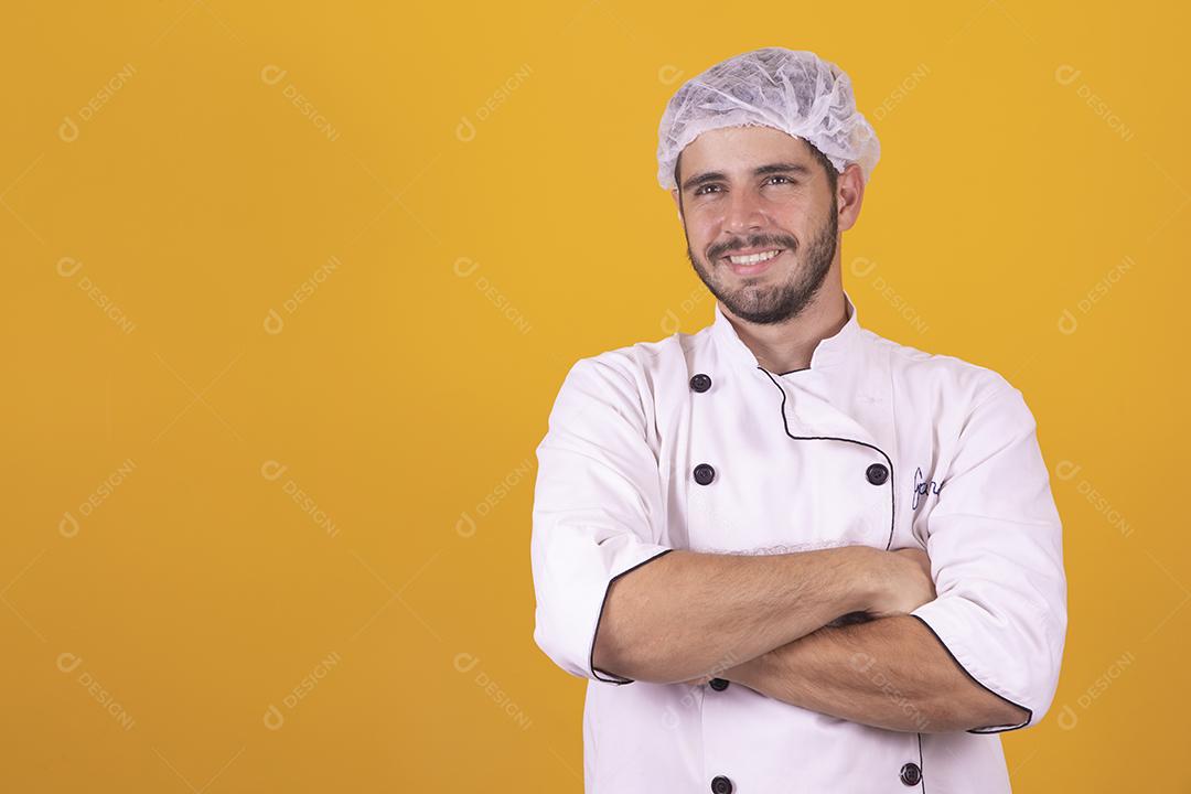 Sorrindo jovem chef masculino cozinheiro ou padeiro na camisa uniforme branca posando isolado no retrato de estúdio de fundo amarelo. Cozinhar o conceito de comida. Mock up espaço de cópia. Chicotear ovos batendo na tigela