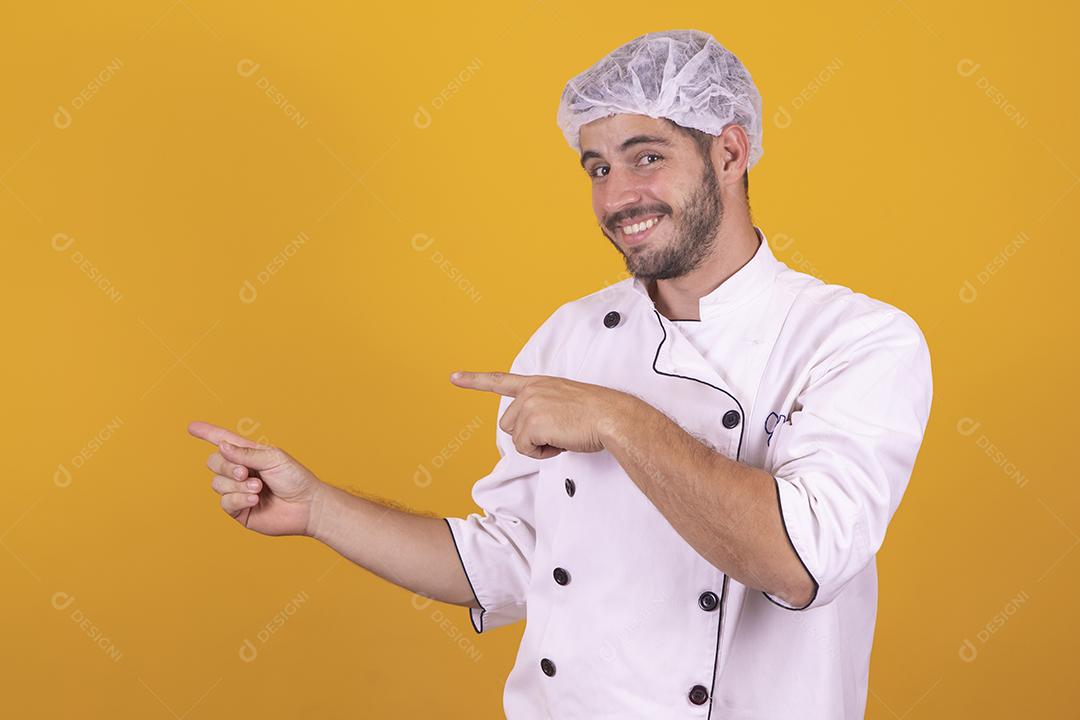 Sorrindo jovem chef masculino cozinheiro ou padeiro na camisa uniforme branca posando isolado no retrato de estúdio de fundo amarelo. Cozinhar o conceito de comida. Mock up espaço de cópia. Chicotear ovos batendo na tigela