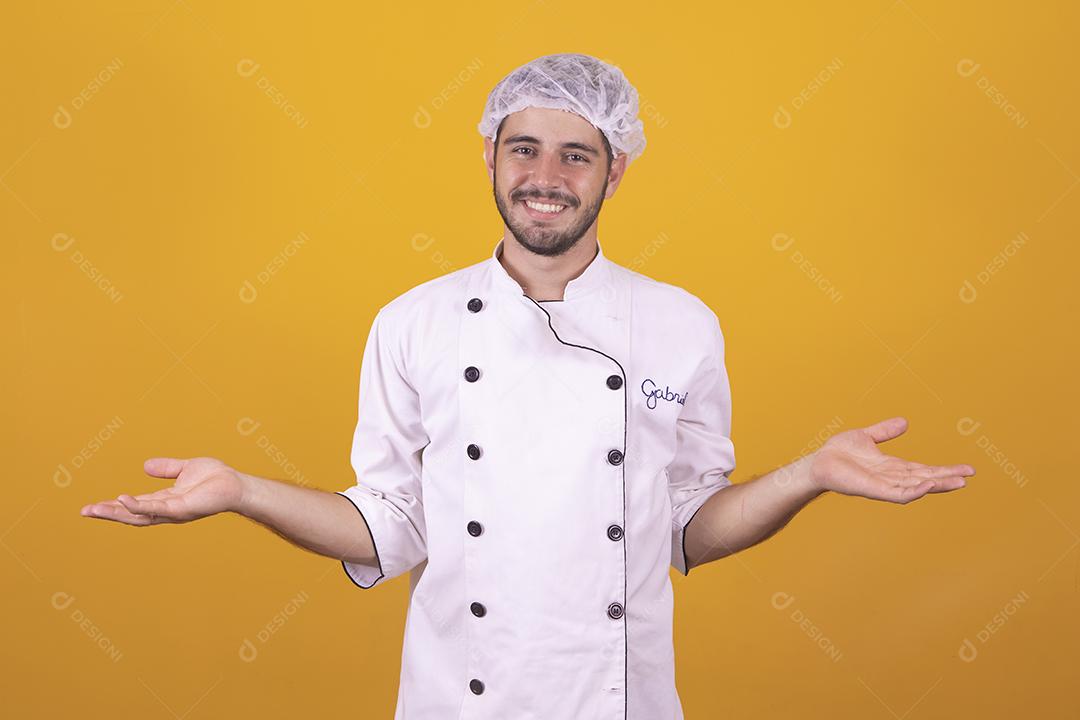 Sorrindo jovem chef masculino cozinheiro ou padeiro na camisa uniforme branca posando isolado no retrato de estúdio de fundo amarelo. Cozinhar o conceito de comida. Mock up espaço de cópia. Chicotear ovos batendo na tigela