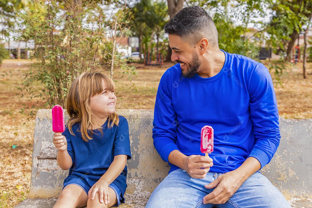 Pai e filha no parque chupando um delicioso picolé