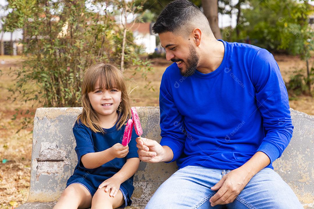 Pai e filha no parque chupando um delicioso picolé