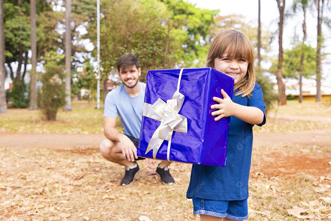 Este presente é para você. Retrato de menina amorosa ao lado do pai cumprimentando-o com o dia dos pais ou aniversário, segurando a caixa de presente embrulhada, feliz feriado em família juntos no parque