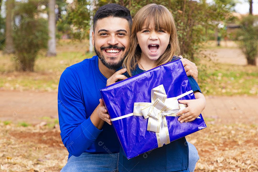 Este presente é para você. Retrato de menina amorosa ao lado do pai cumprimentando-o com o dia dos pais ou aniversário, segurando a caixa de presente embrulhada, feliz feriado em família juntos no parque