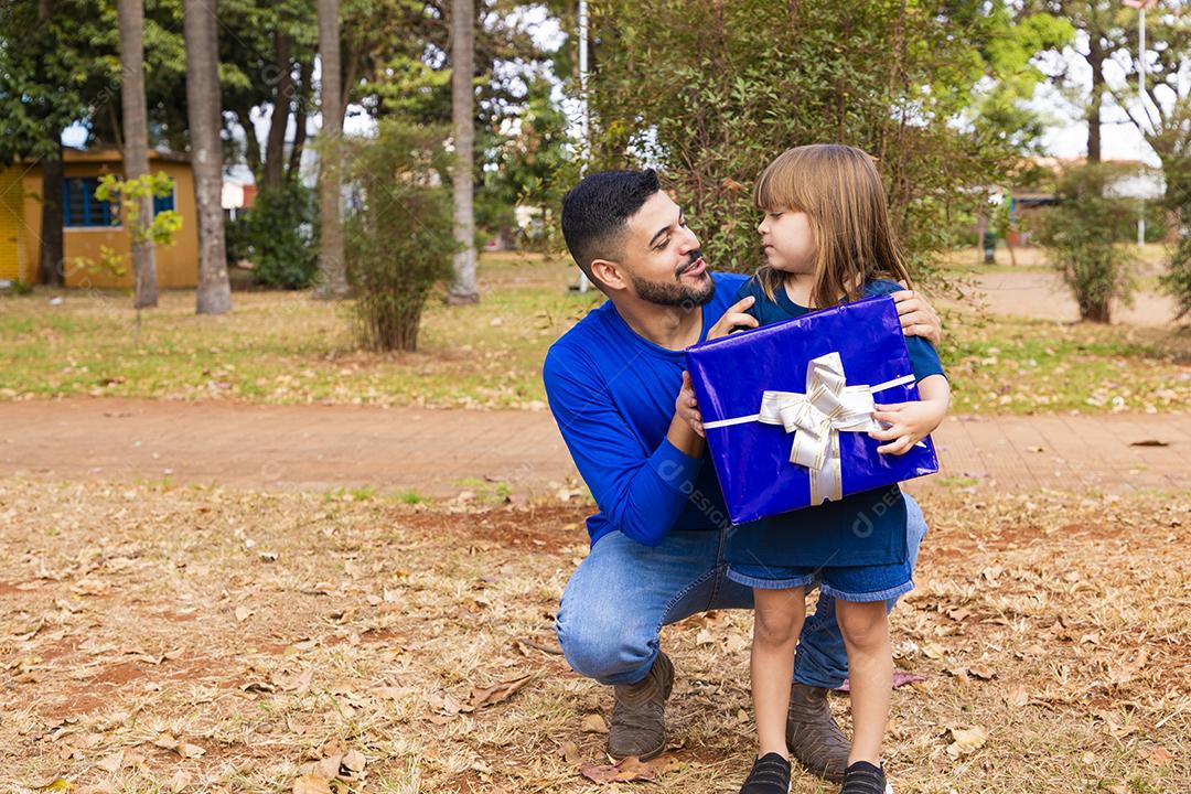Este presente é para você. Retrato de menina amorosa ao lado do pai cumprimentando-o com o dia dos pais ou aniversário, segurando a caixa de presente embrulhada, feliz feriado em família juntos no parque