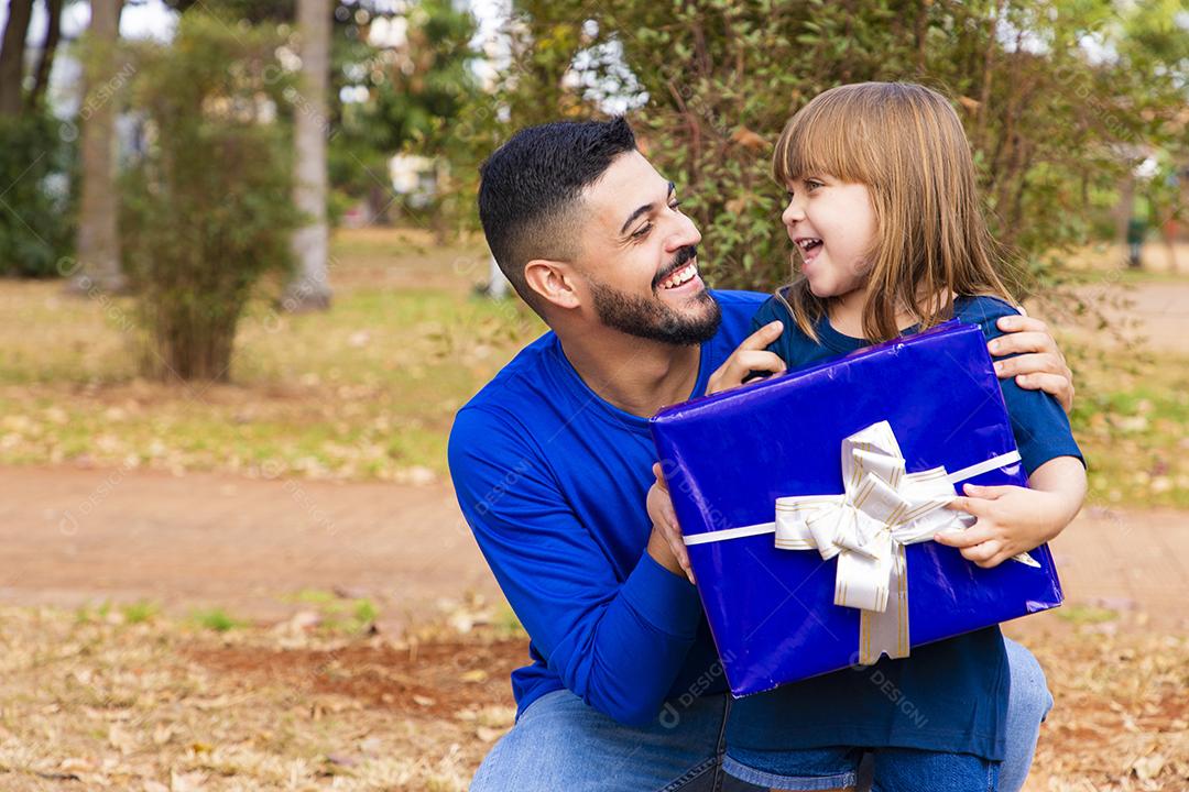 Este presente é para você. Retrato de menina amorosa ao lado do pai cumprimentando-o com o dia dos pais ou aniversário, segurando a caixa de presente embrulhada, feliz feriado em família juntos no parque
