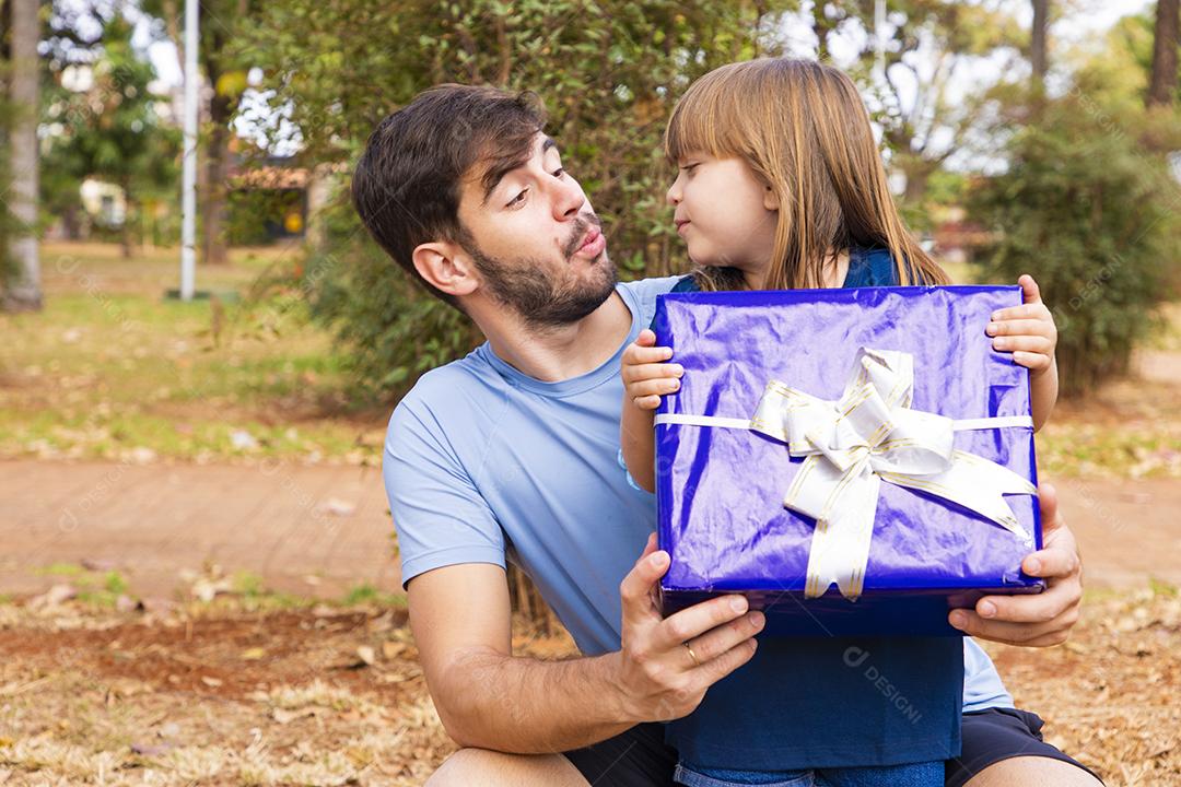 Este presente é para você. Retrato de menina amorosa ao lado do pai cumprimentando-o com o dia dos pais ou aniversário, segurando a caixa de presente embrulhada, feliz feriado em família juntos no parque