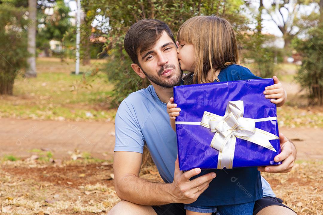 Este presente é para você. Retrato de menina amorosa ao lado do pai cumprimentando-o com o dia dos pais ou aniversário, segurando a caixa de presente embrulhada, feliz feriado em família juntos no parque