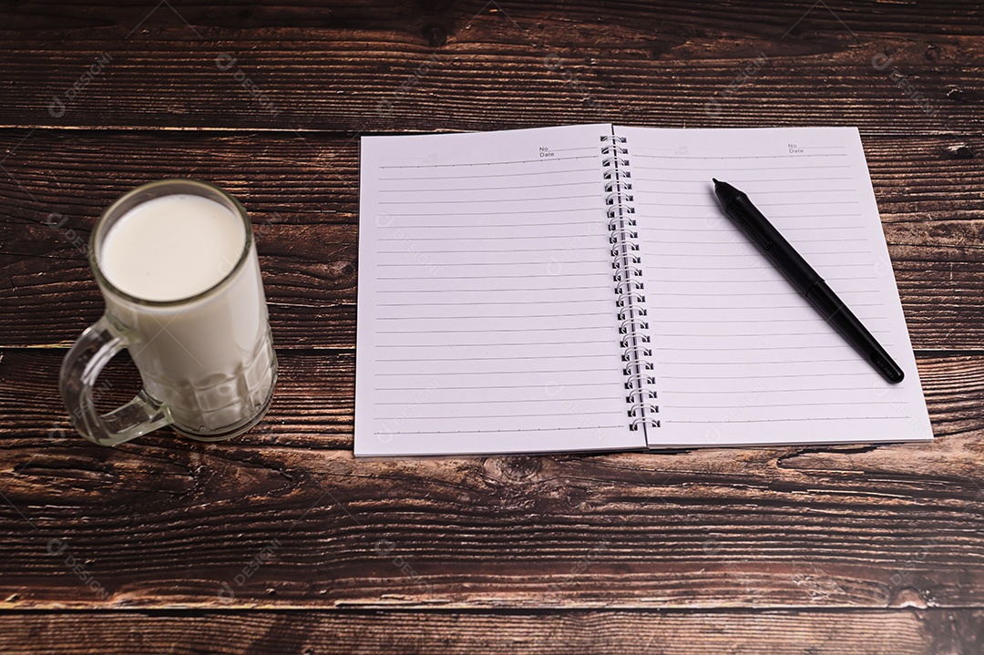 Caderno e um copo de leite estão sobre a mesa.