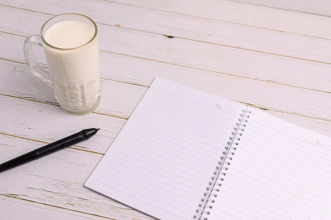 Caderno e um copo de leite estão sobre a mesa.