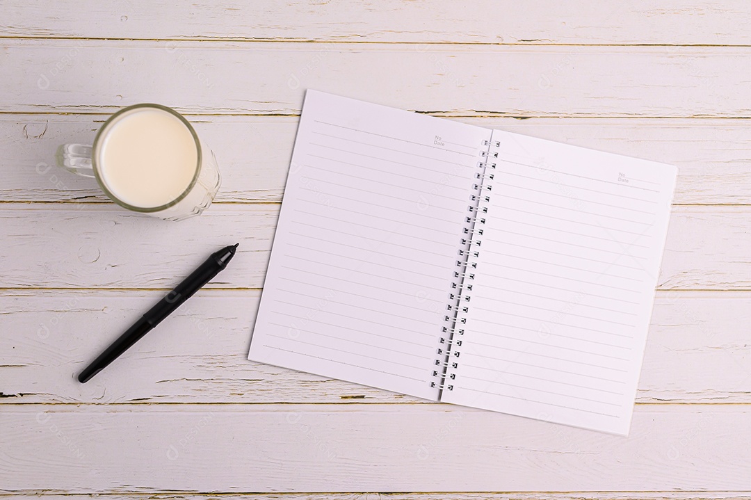 Caderno e um copo de leite estão sobre a mesa.
