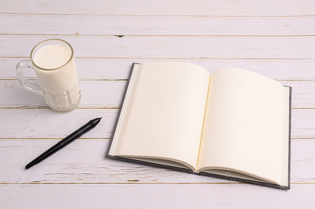 Caderno e um copo de leite estão sobre a mesa.