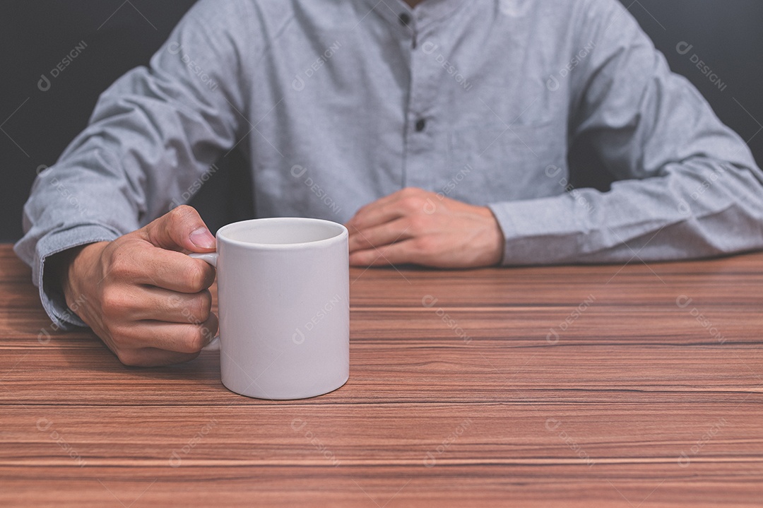 Homem segurando uma xícara de café em sua mesa